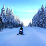 Snowmobiling on Snowmobiling on a Snowy Mountain Road with Snow Covered Pine Trees